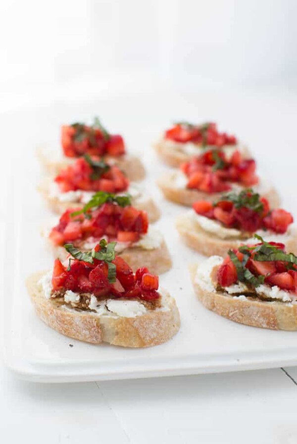 eight slices of strawberry bruschetta sitting on a white plate on a white table