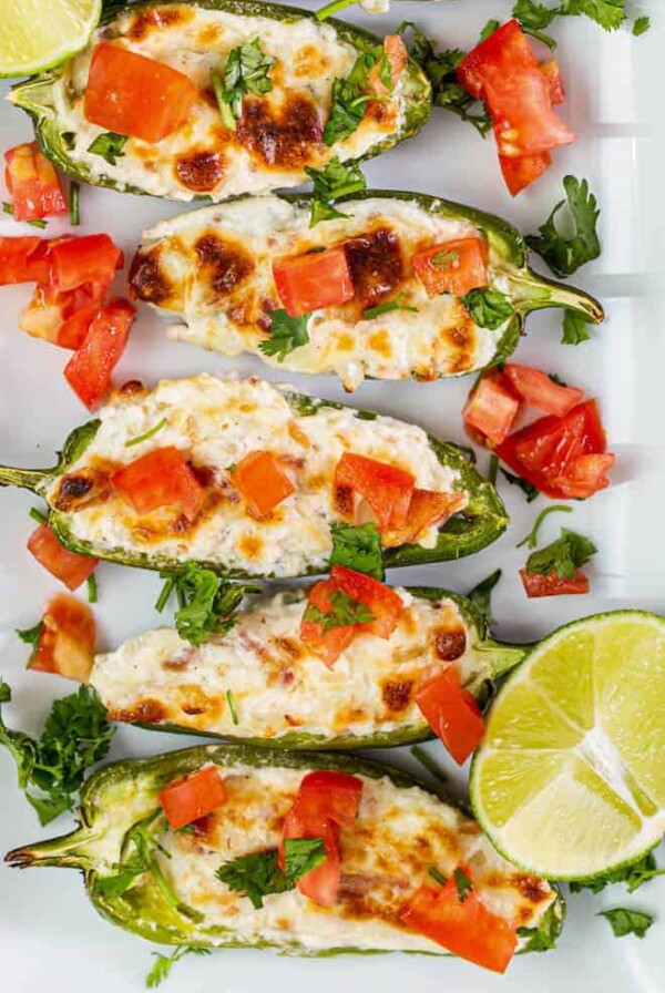 Five stuffed jalapenos sitting on a white plate.