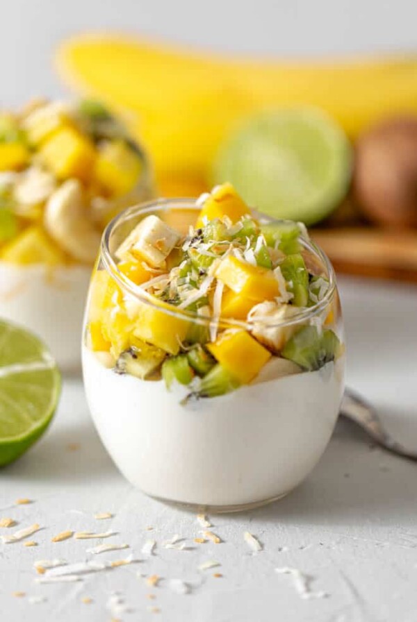 clear glass jar filled with greek yogurt with mango, kiwi, banana and pineapple chunks piled on top