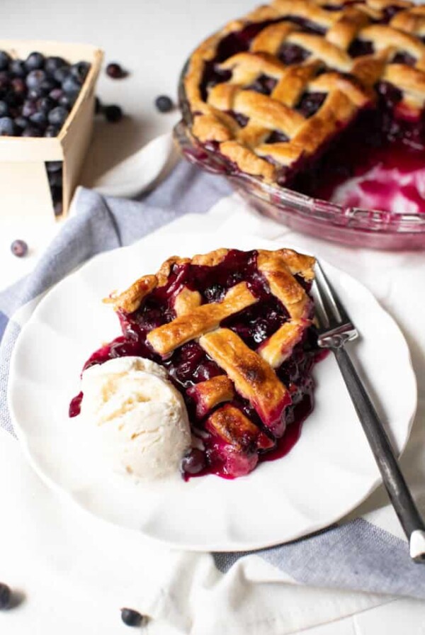 a slice of blueberry pie with a scoop of ice cream on a white plate with a fork