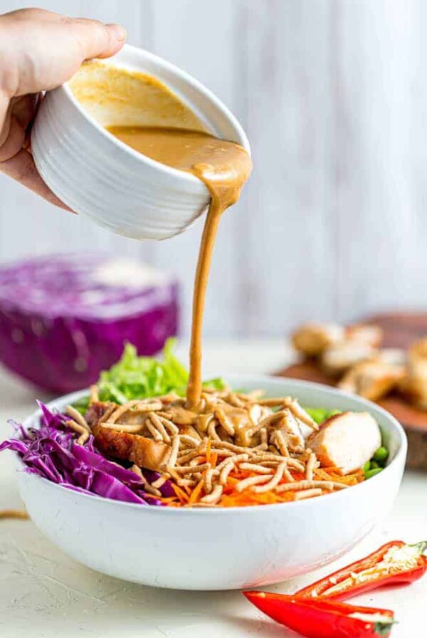 Pouring peanut sauce into a bowl of thai chicken salad.