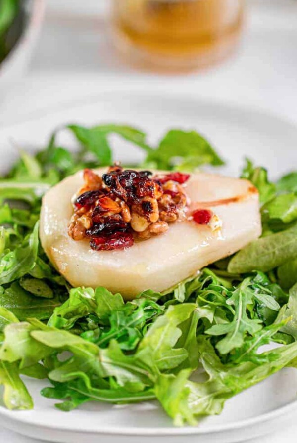 Roasted pear with blue cheese, cranberries and walnuts sitting on a bed of arugula on a plate.