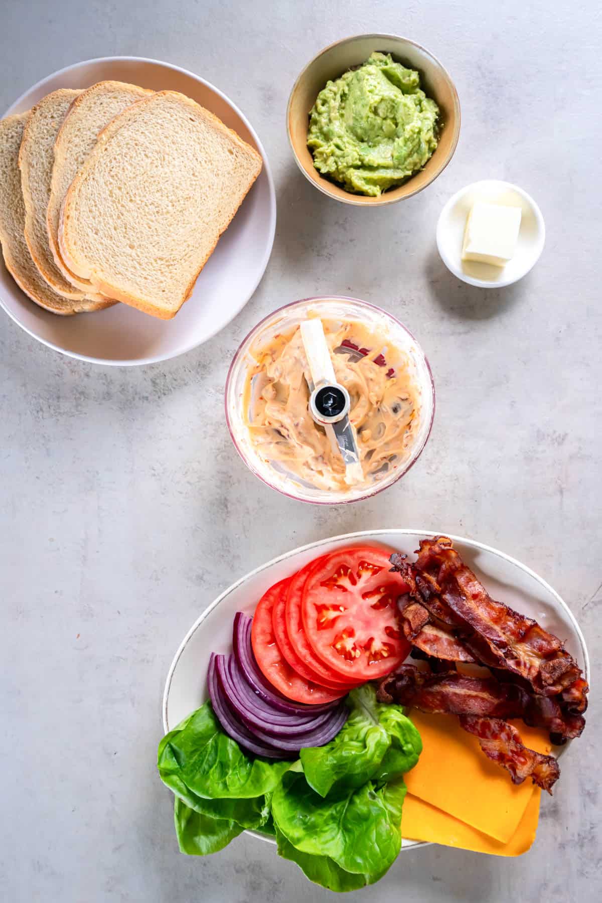 All of the ingredients for BLT grilled cheese on a plate or in bowls on a countertop ready to be made into the sandwich.