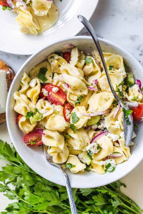 A bowl of tortellini pasta salad with tomatoes, onions and parsley.