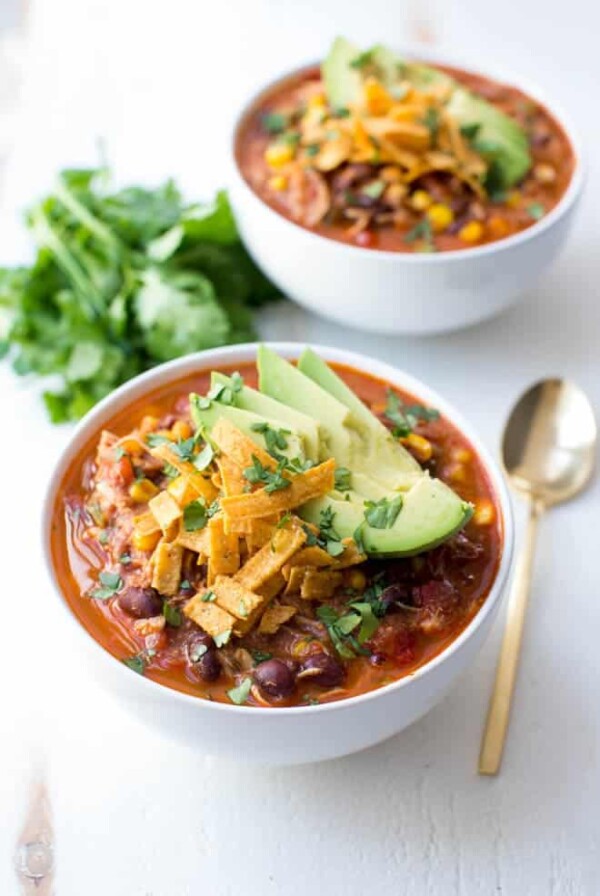 two bowls of chicken enchilada soup sitting on a white table with a spoon on the side