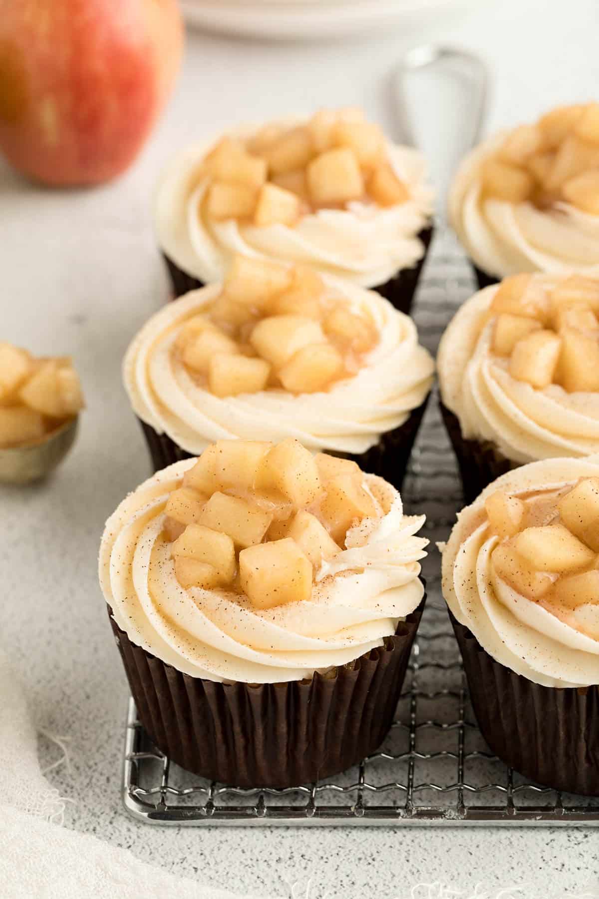 Six apple pie cupcakes sitting on a baking rack after being fully assembled.