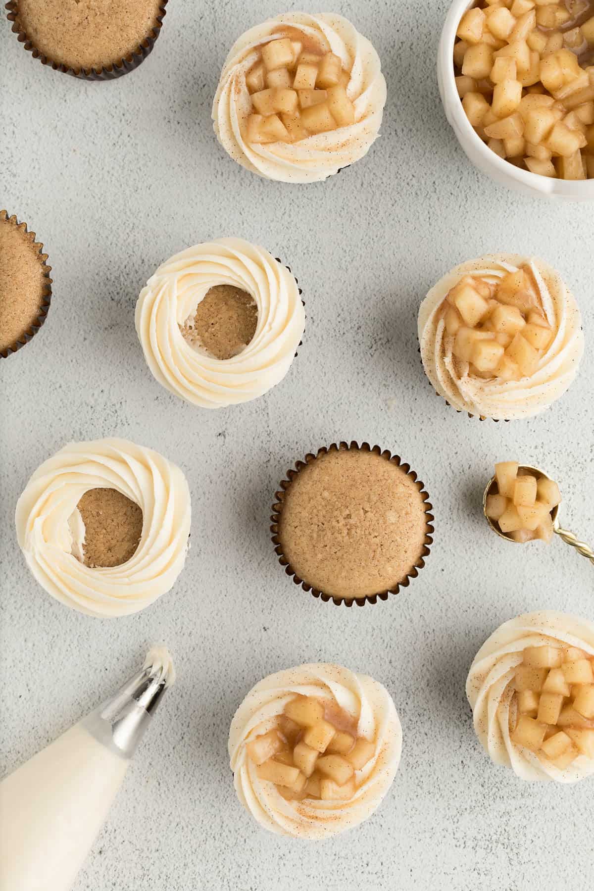 Cupcakes sitting on a white countertop, some with frosting on them during assembly. 