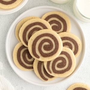 Chocolate and Vanilla Swirl Cookies sitting on a white plate for serving with two glasses of milk on the side.