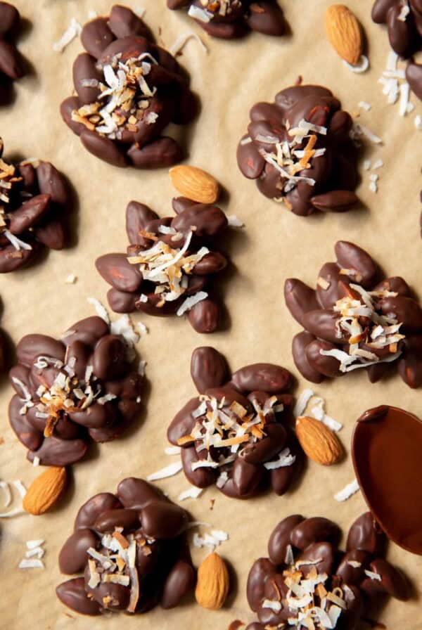 dark chocolate almond clusters on a piece of parchment paper with shredded coconut on top