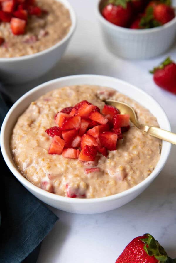 A bowl of strawberry oatmeal with fresh strawberries on top.