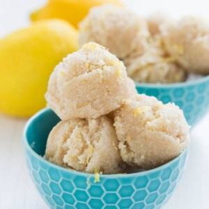 three vegan lemon macaroon sitting in a blue cut on a white background with two lemons in the background