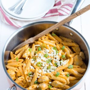 a pan with buffalo chicken pasta sitting on a white table with a spoon in it