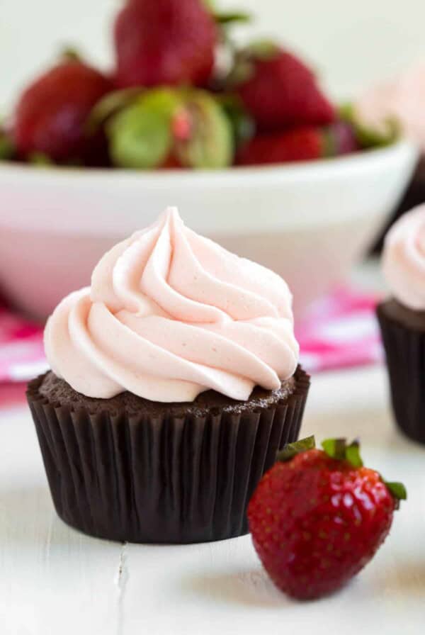 one chocolate strawberry cupcake sitting in front of a bowl of strawberries