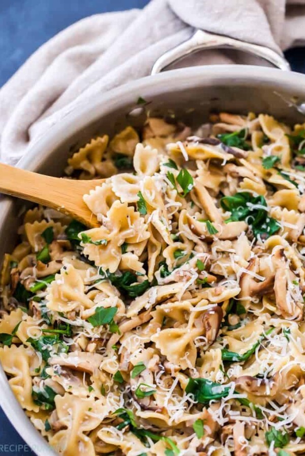 a wooden spoon scooping out spinach and mushroom pasta