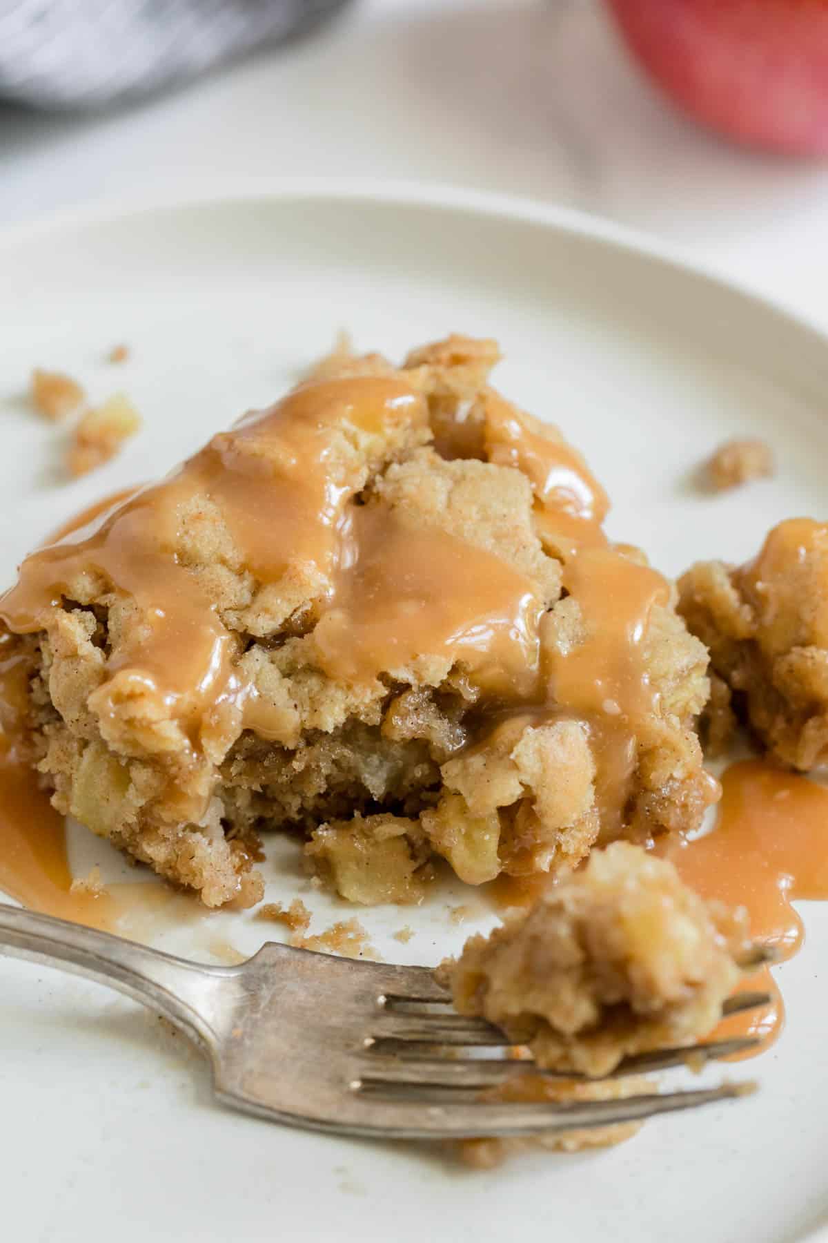 A fork with a piece of apple cake on a plate with caramel drizzle.