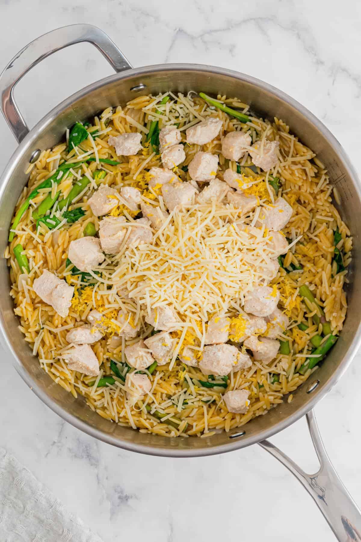 A Pan of Lemon Chicken Orzo with spinach, asparagus, and lemon wedges with cheese sprinkled on top.