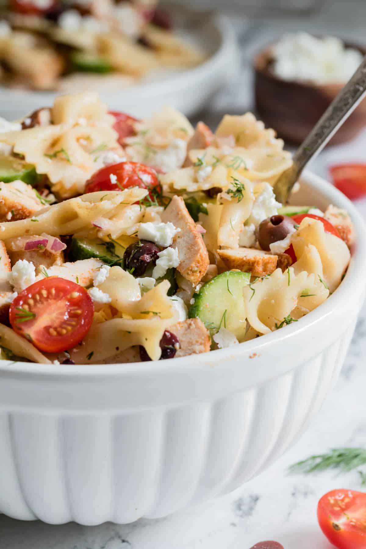 A large serving spoon scoops the greek chicken pasta salad from the bowl. 