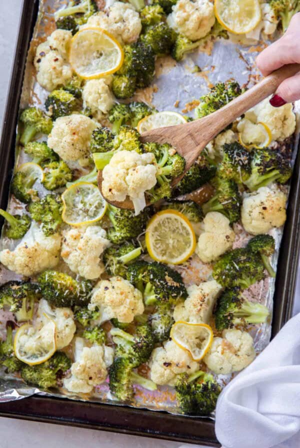 A spoon scooping roasted broccoli and cauliflower off the pan.