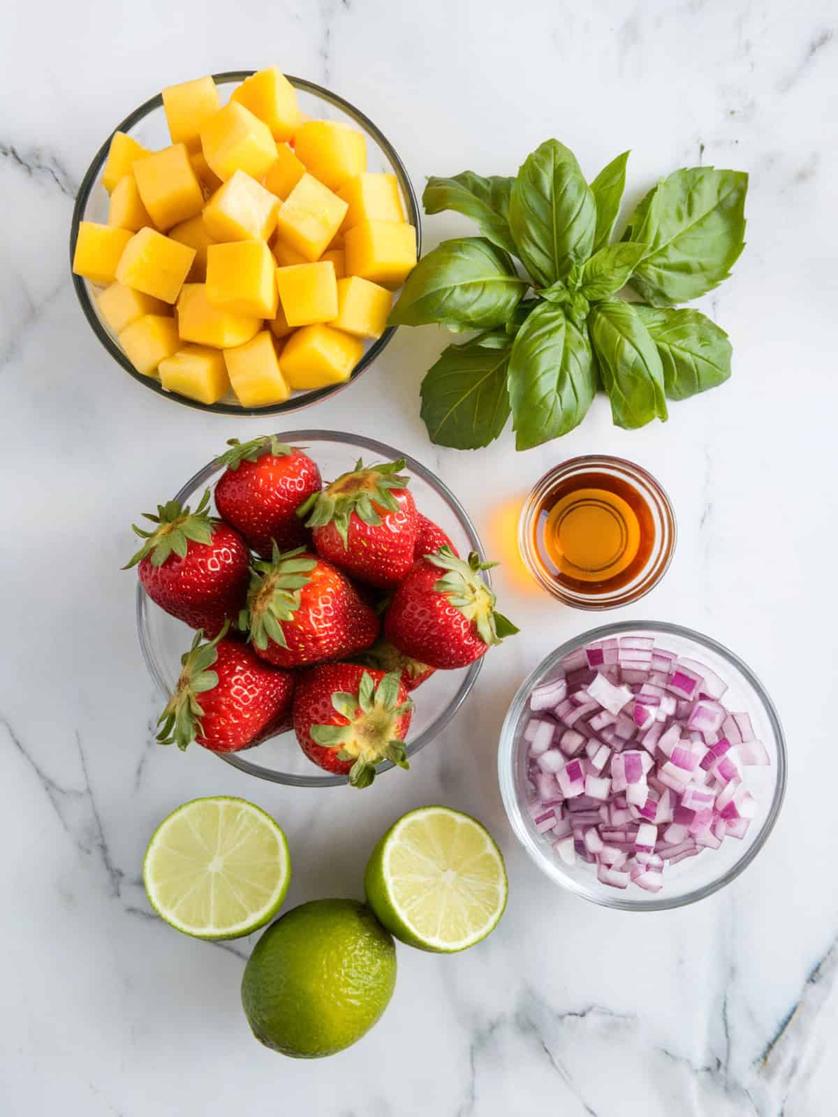 An overhead shot of ingredients for strawberry mango salsa sitting on a white marble countertop.