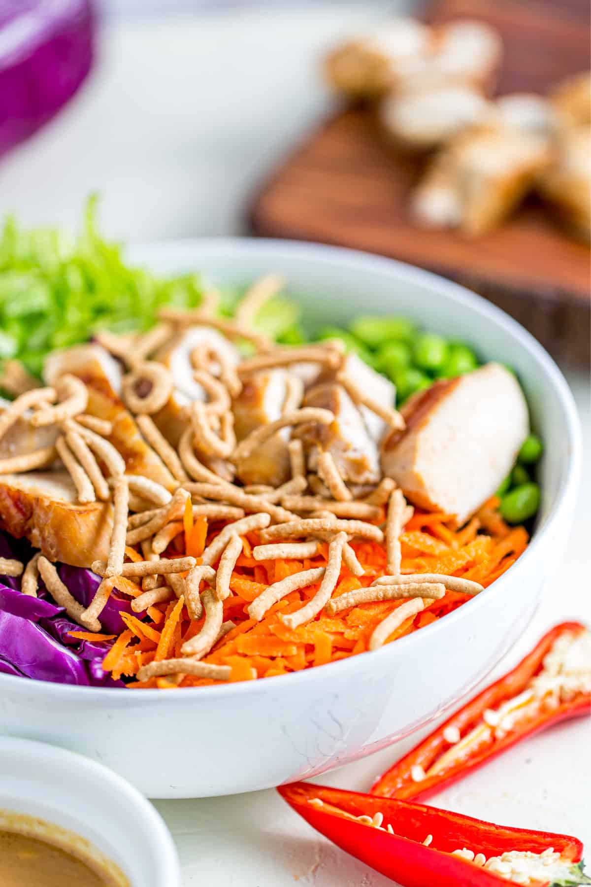 A bowl of Thai Chicken Salad with red peppers next to it.