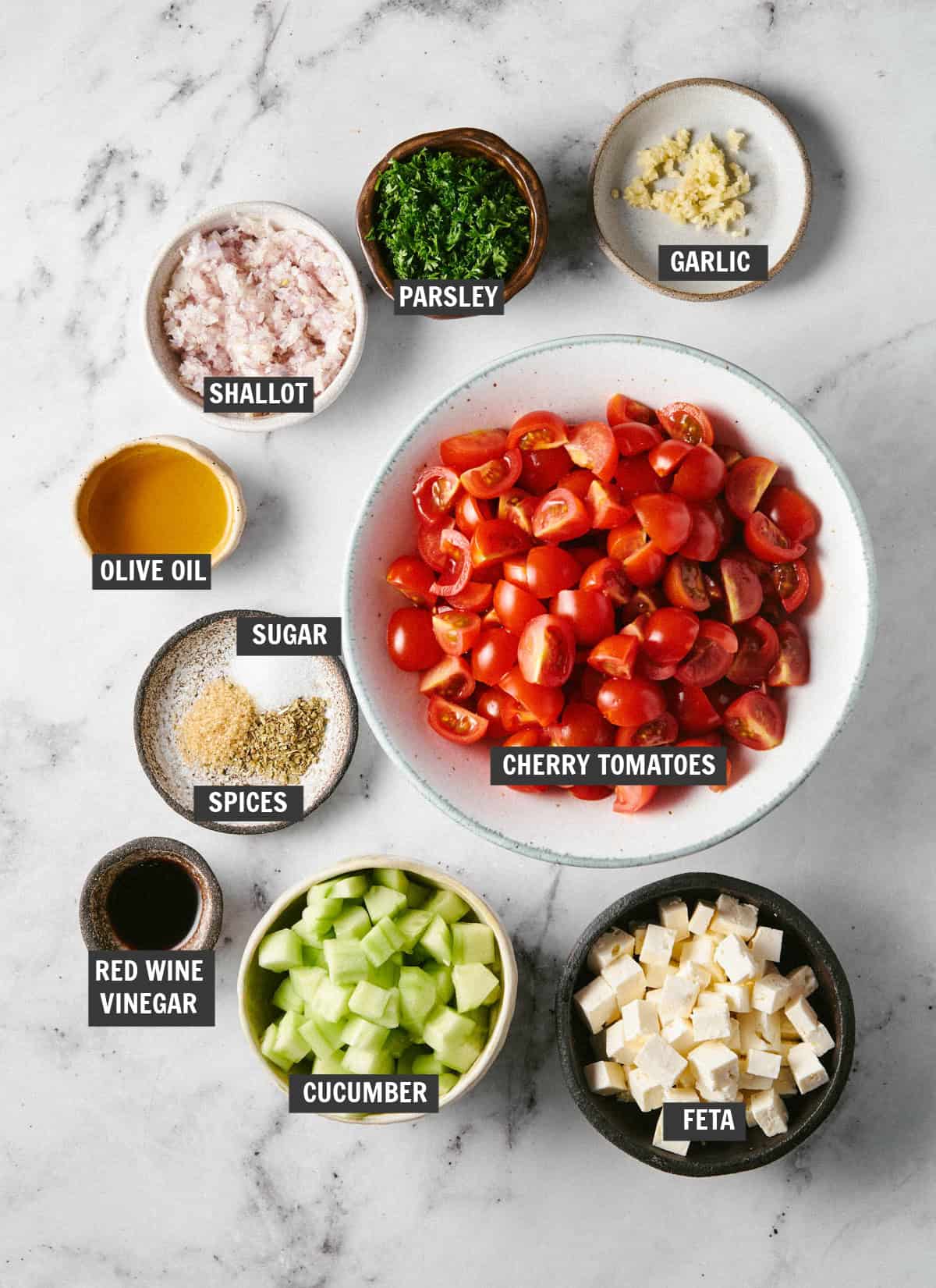 All of the ingredients for Mediterranean cucumber and tomato salad in bowls on a countertop. 