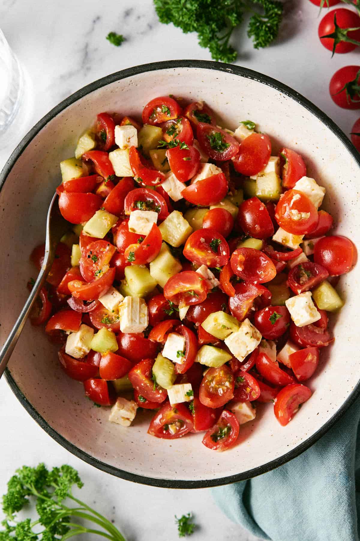 Mediterranean Cucumber and Tomato Salad with Feta in a bowl with a serving spoon sitting on a countertop ready for serving. 