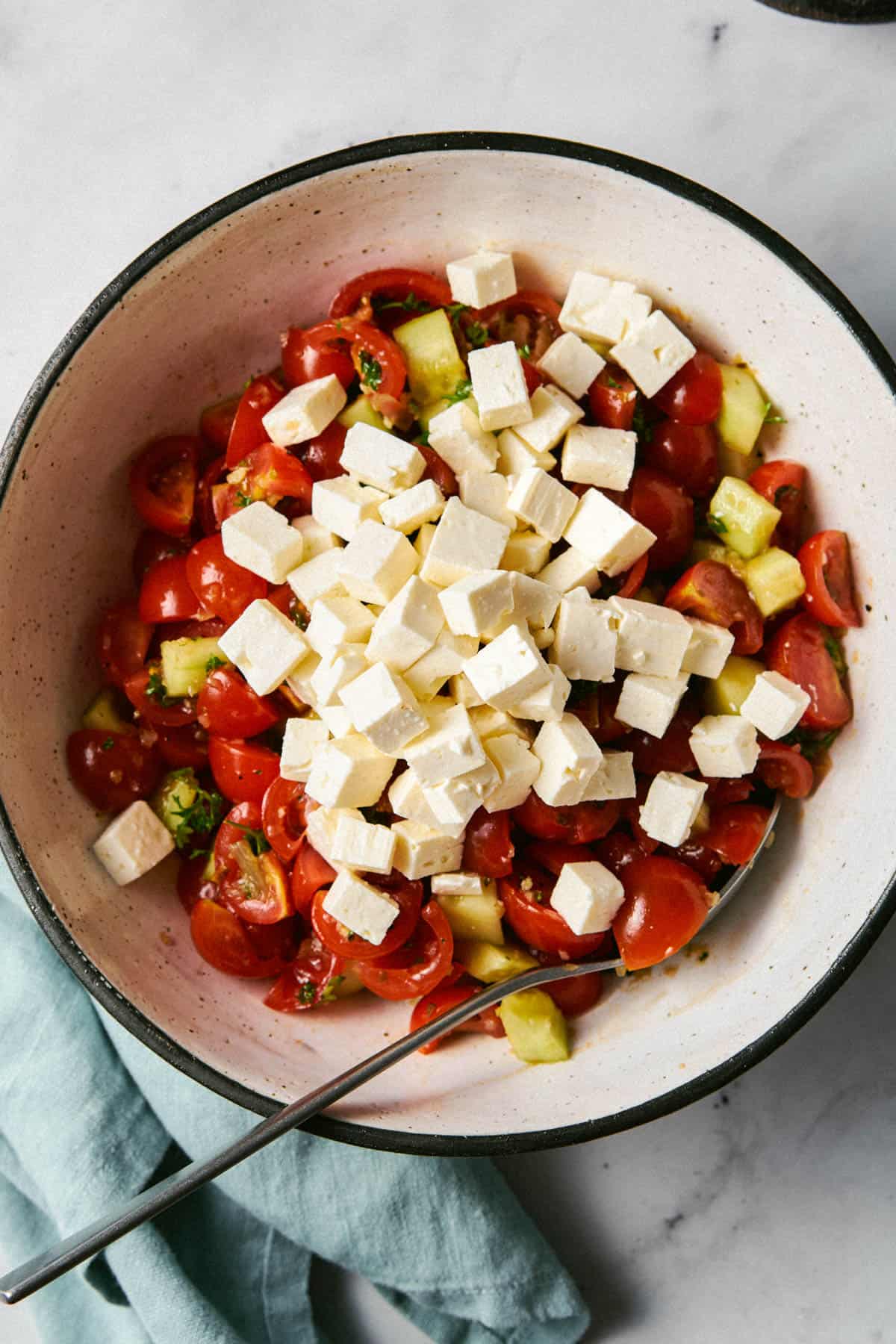 Cucumber and tomato salad in a bowl with cubed feta on top before mixing and serving. 