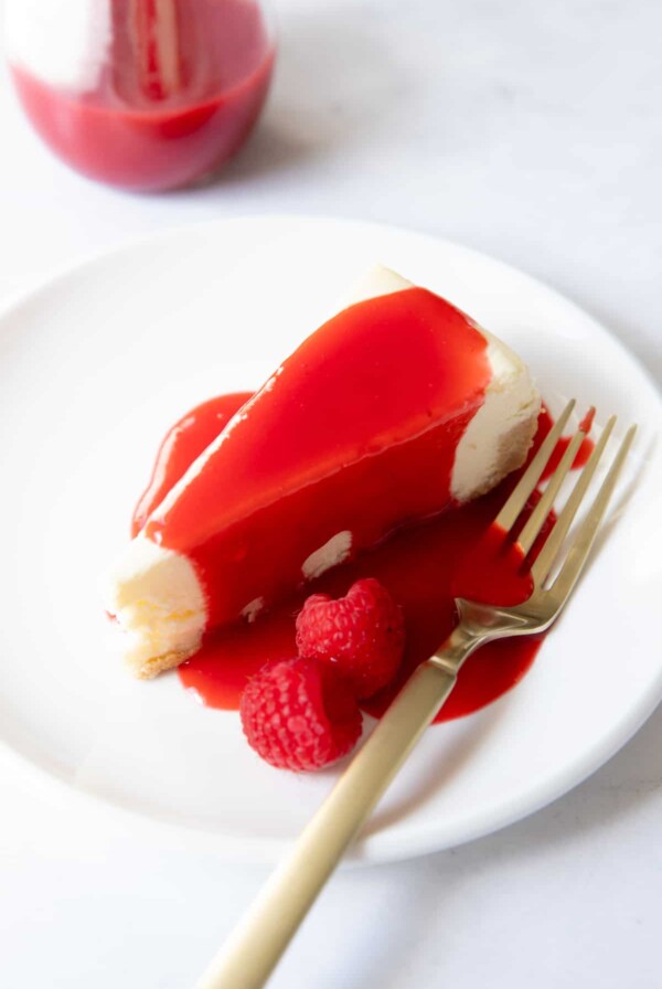 a piece of cheesecake on a plate with raspberry sauce on it