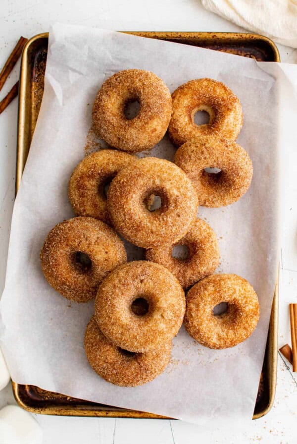 a pile of apple cider donuts on a piece of parchment paper on a baking sheet