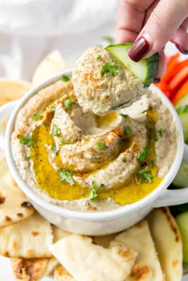 A cucumber digging into a bowl of homemade baba ghanouj