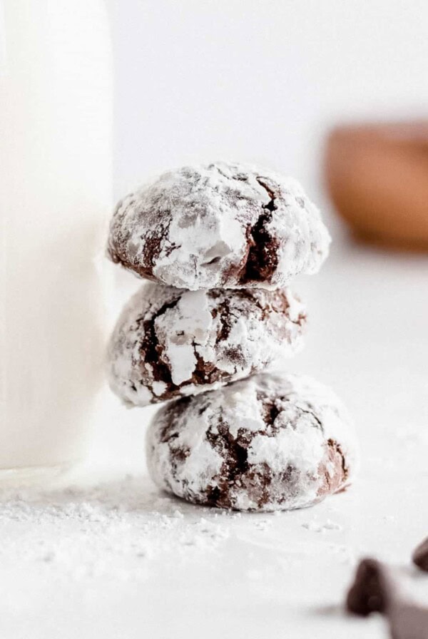 a stack of three chocolate crinkle cookies sitting next to a glass of milk