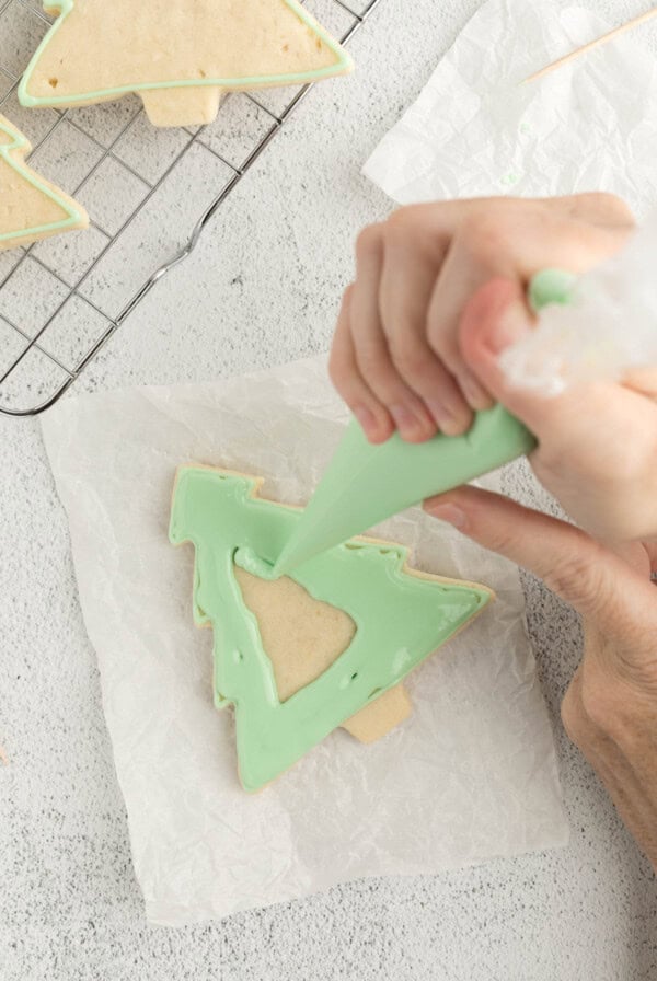 holding a piping bag in one hand to fill the cookies with royal icing