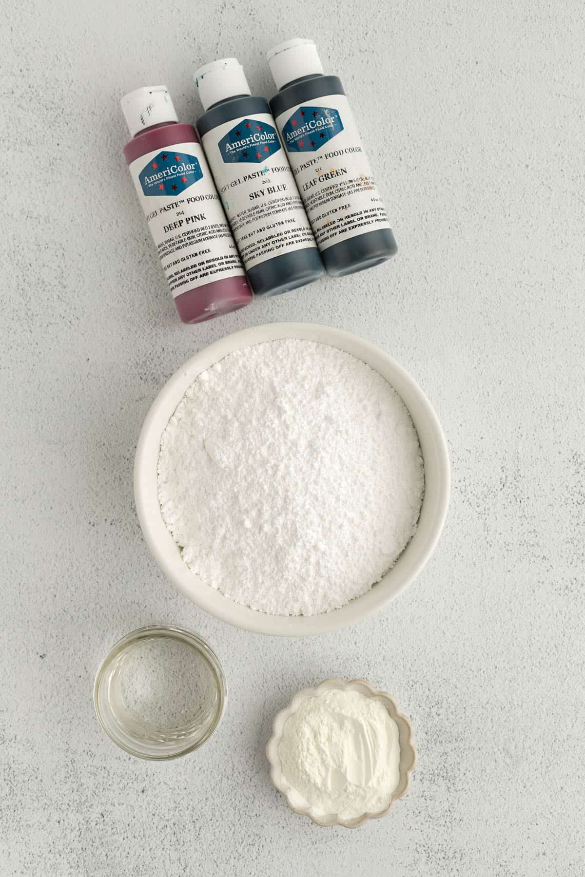 All of the ingredients for royal icing in bowls on a white countertop. 