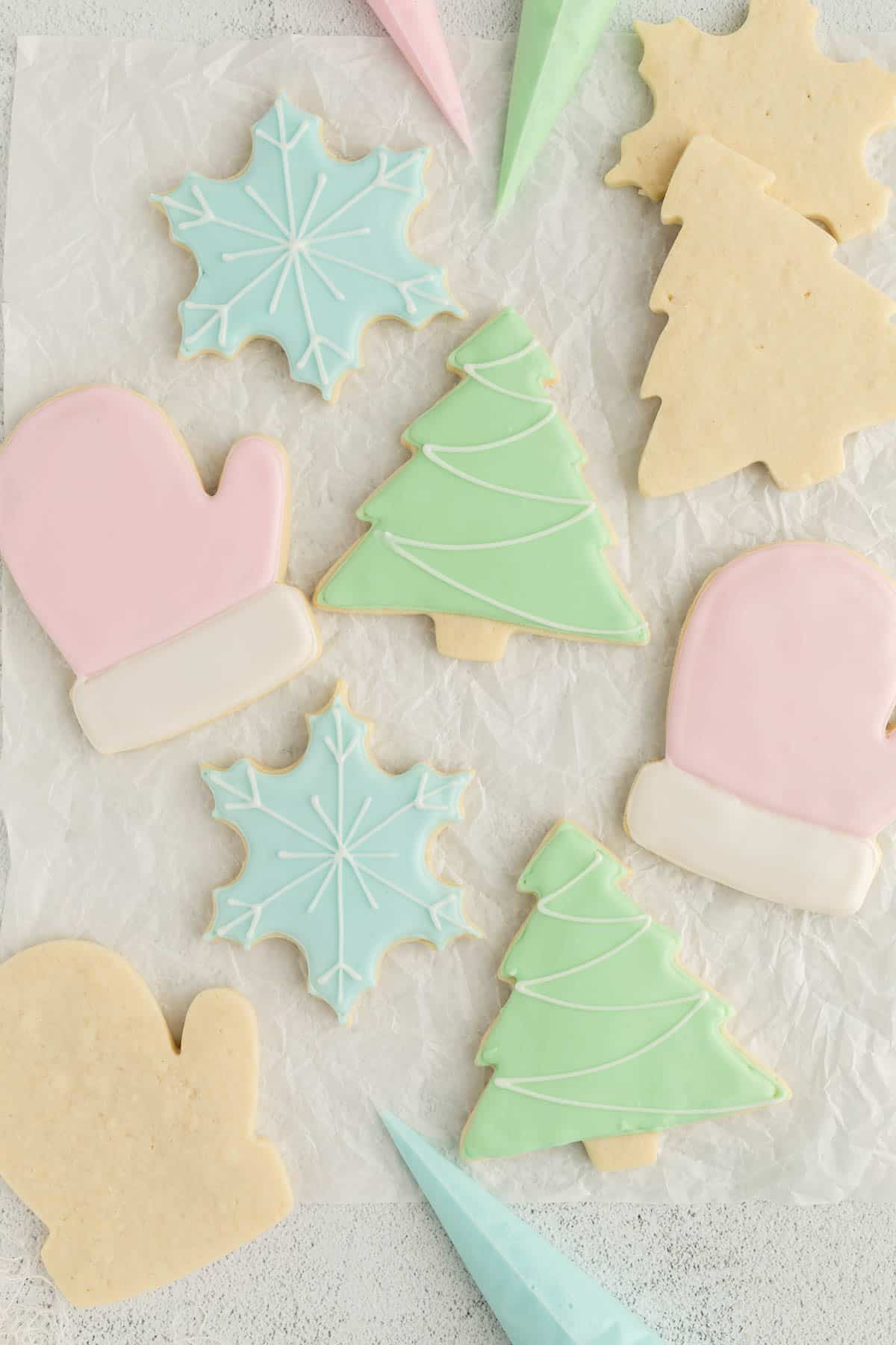 Sugar cookies decorated with royal icing sit on white parchment paper after decorating. 