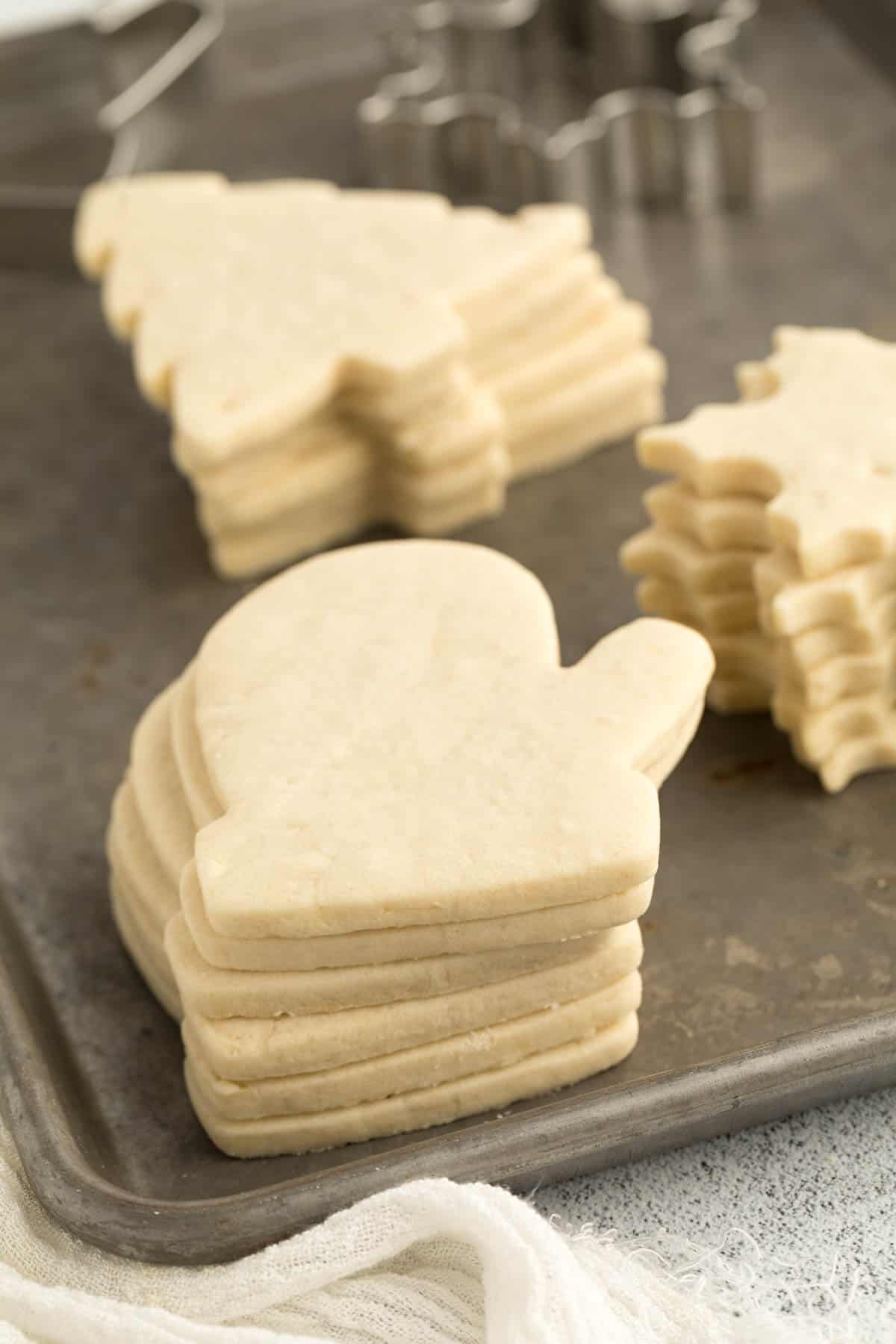 Cut out sugar cookies stacked on a baking sheet ready to be decorated. 