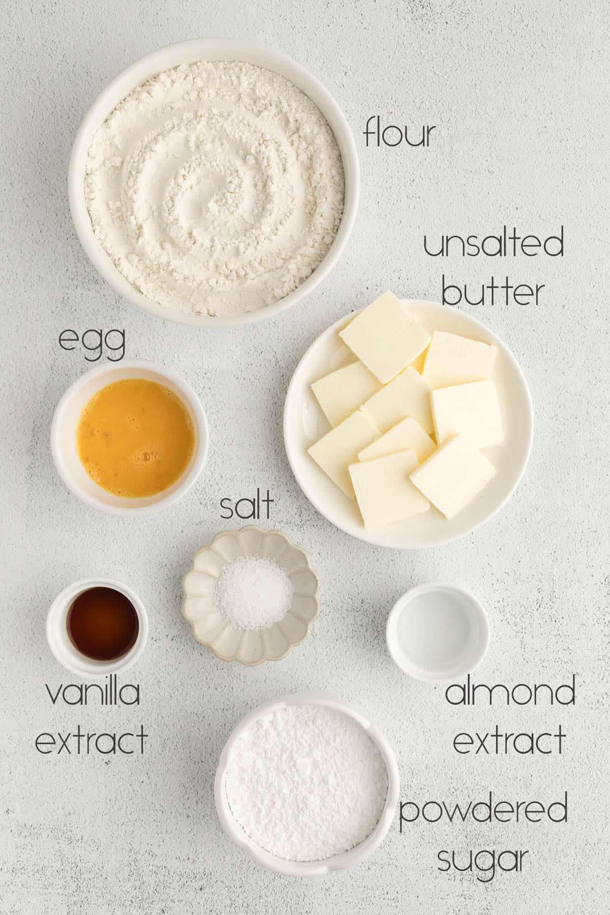 All of the ingredients for cut out sugar cookies in bowls on a white countertop.