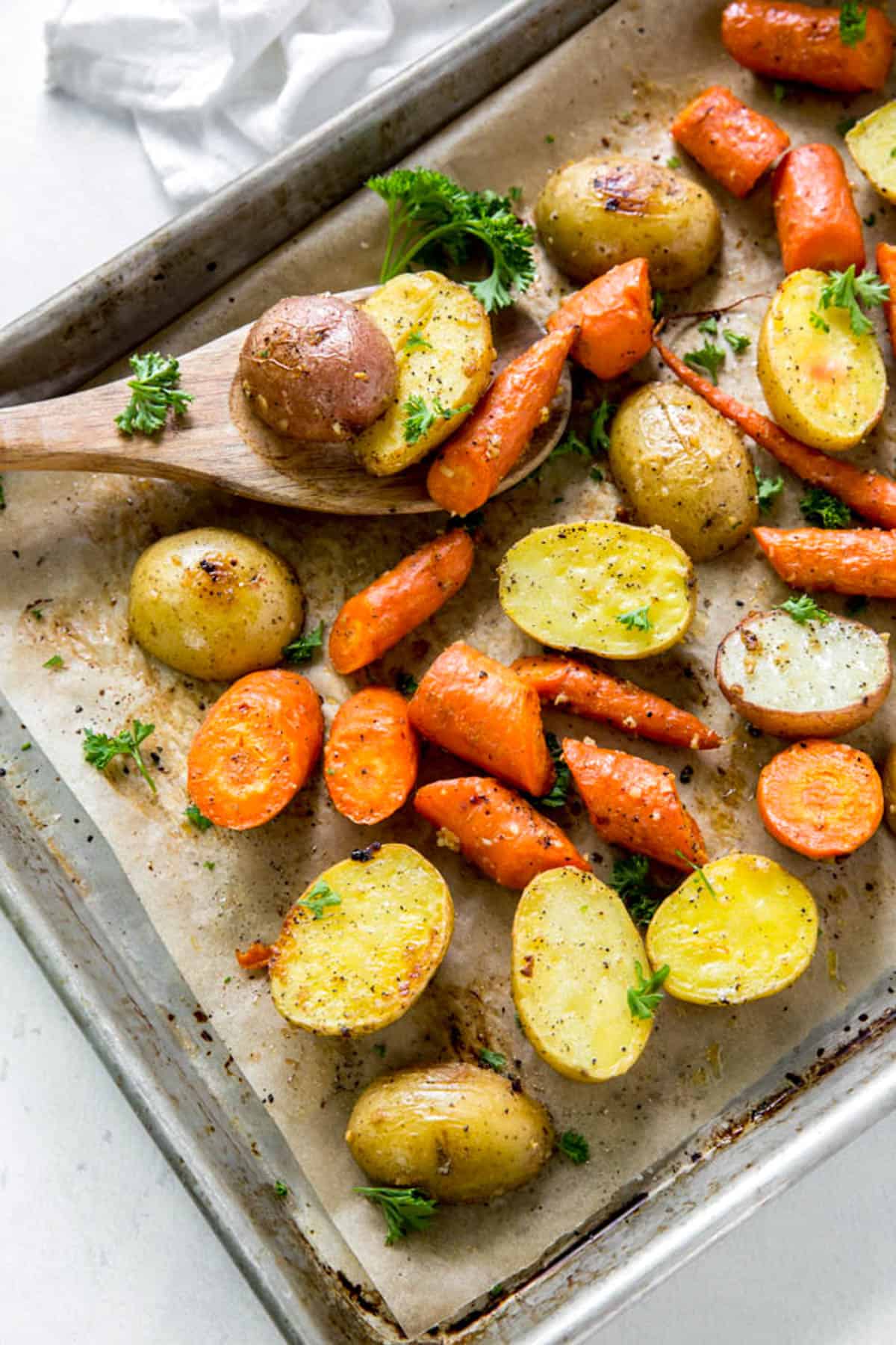 Pan with roasted potatoes and carrots garnished with parsley and wood serving spoon.