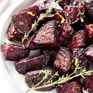 Oven roasted beets on a white plate after roasting in the oven. A piece of thyme is garnished on the side.