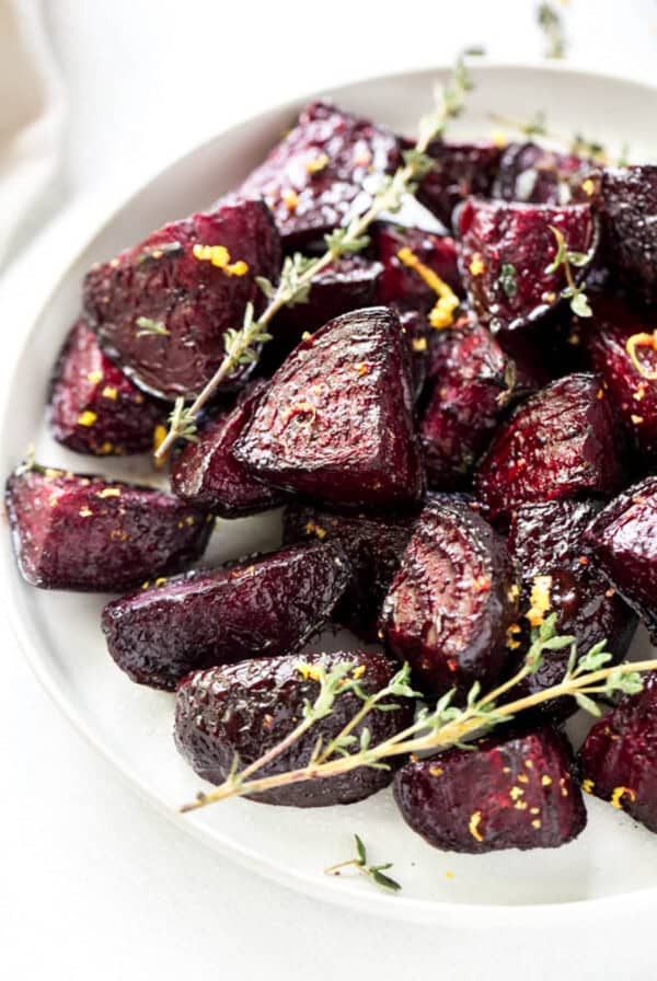 Oven roasted beets on a white plate after roasting in the oven. A piece of thyme is garnished on the side.