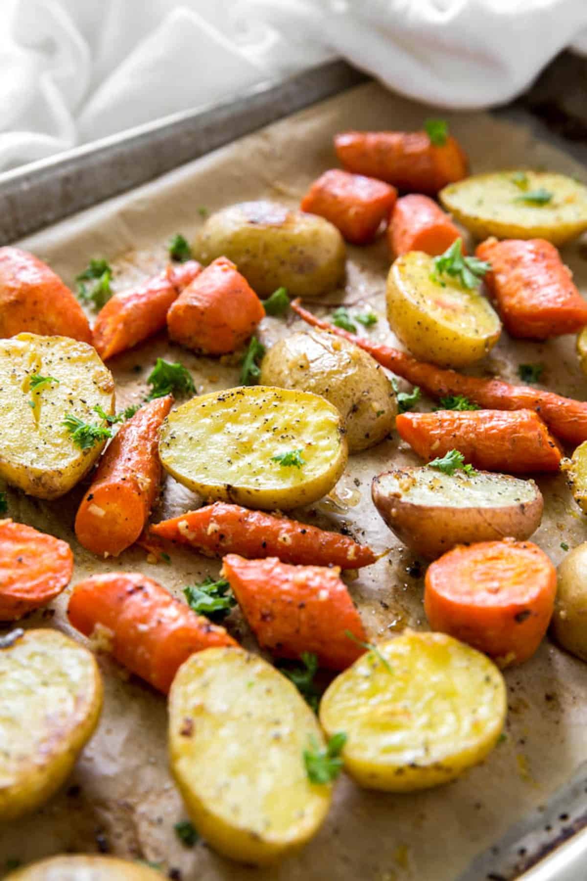 An angled view of roasted potatoes and carrots garnished with parsley on a a roasting pan and parchment paper.