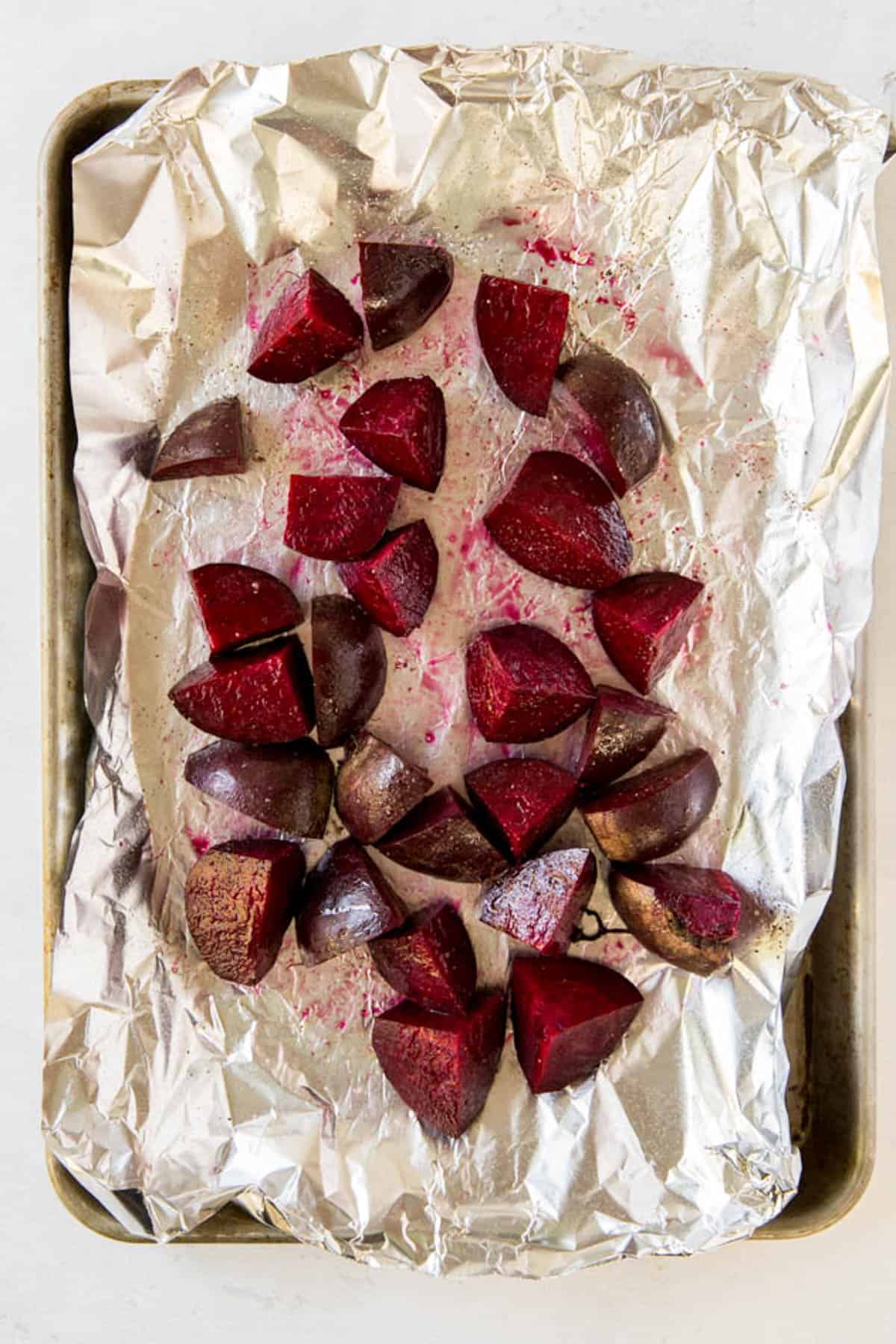 Raw cut beets on a piece of aluminum foil on a sheet pan before baking. 