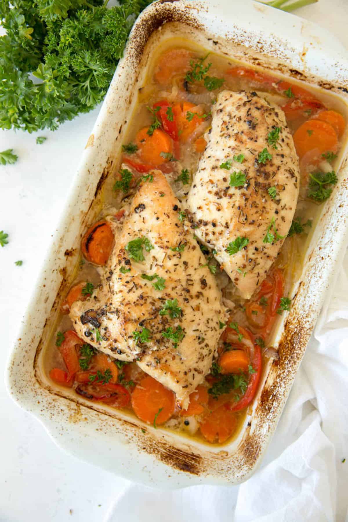 Baked turkey tenderloin with carrots, onions and red peppers in a white baking dish after cooking in the oven.