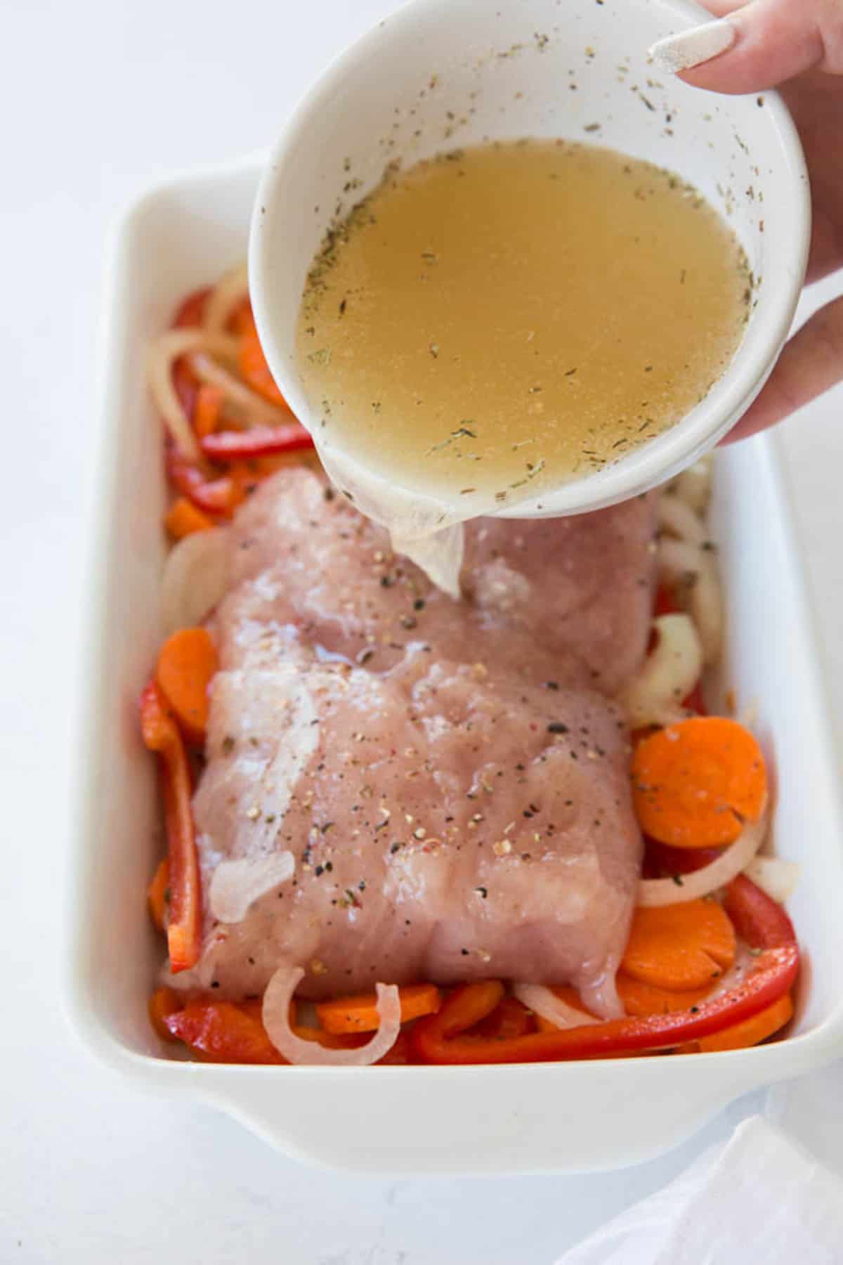 Pouring the broth and wine mixed with the seasonings over the turkey tenderloin in the baking dish before cooking.