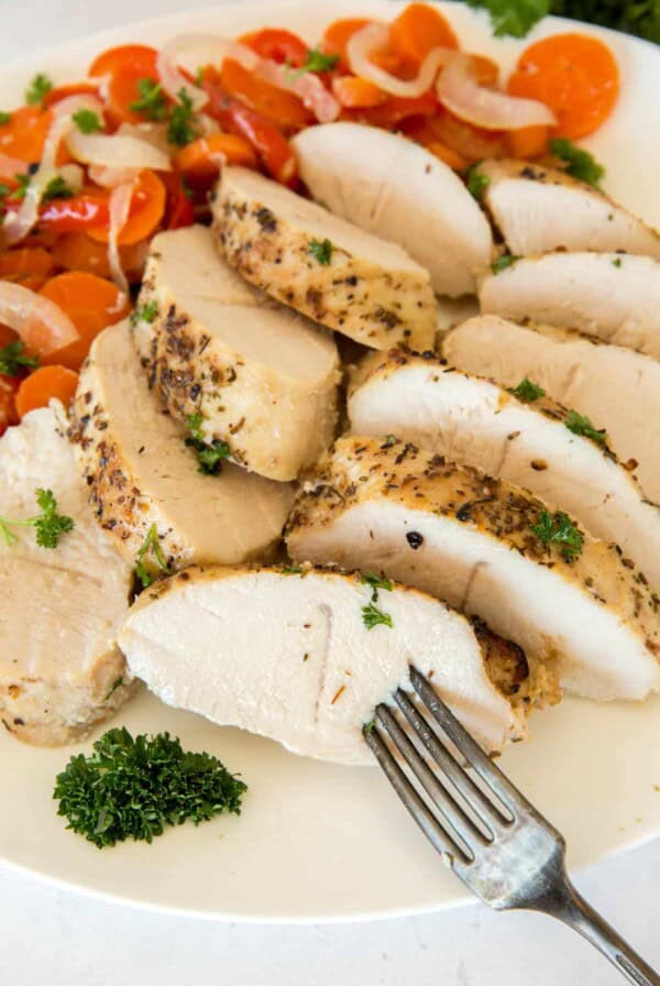 Sliced baked turkey tenderloin on a plate with the cooked carrots, peppers and onions. A fork sticks into a piece of turkey tenderloin before eating.