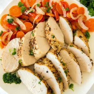 Sliced baked turkey tenderloin on a plate with the cooked carrots, onions and bell peppers for serving.