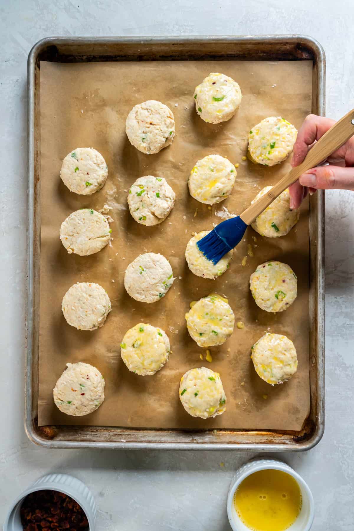 A hand uses a pastry brush to brush the top of the scones with egg wash. 