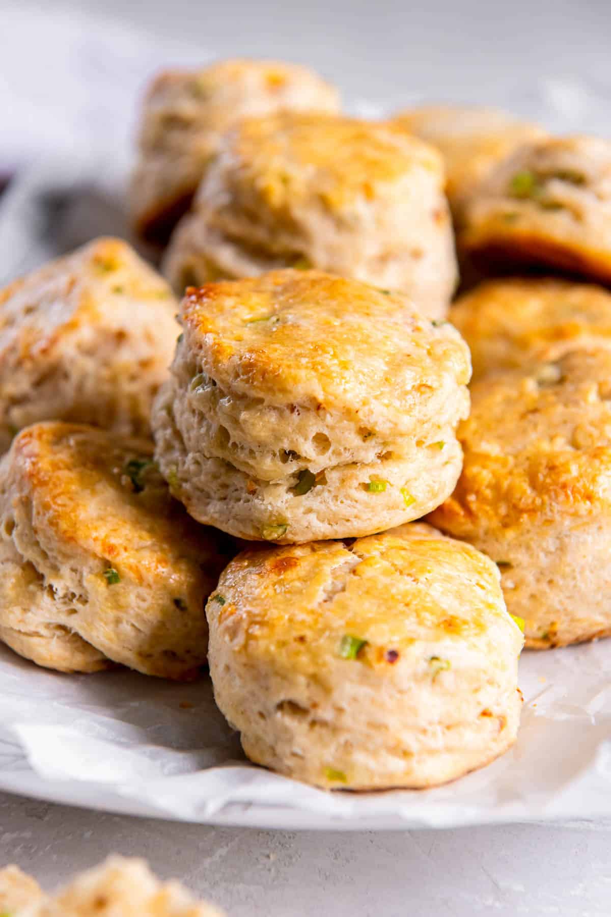 A white plate stacked with cheddar scones with chives. 