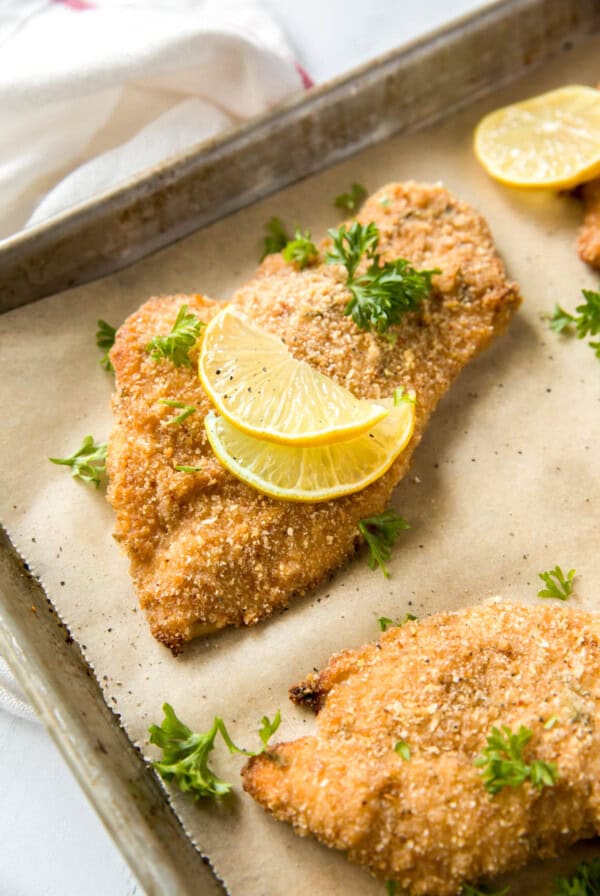 A few baked chicken cutlets on a baking sheet after baking in the oven.