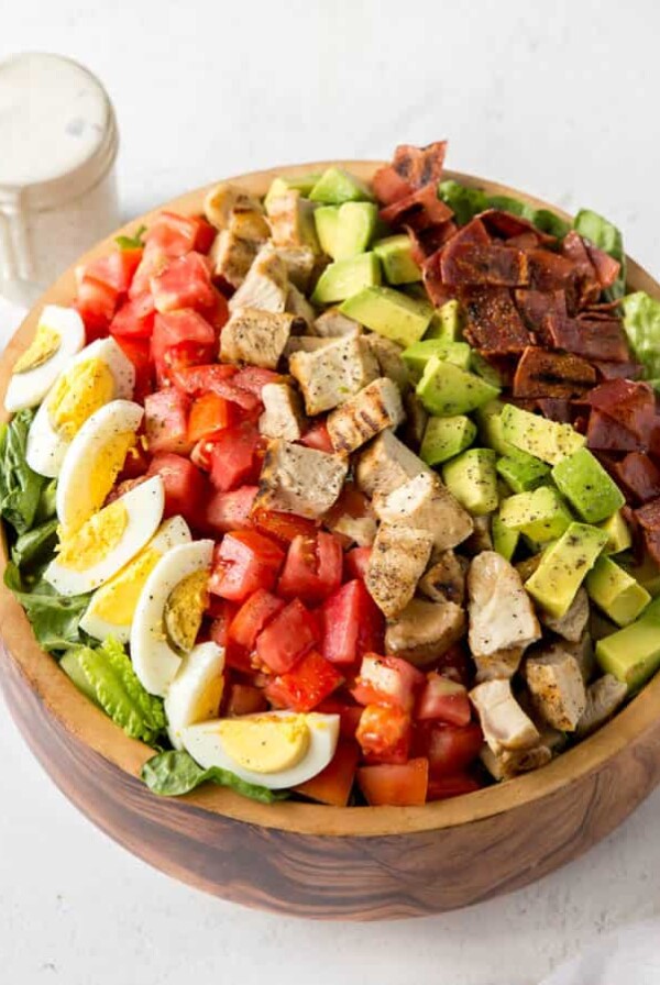 a large wooden bowl with lettuce, boiled egg, tomatoes, grilled turkey, avocado and turkey bacon