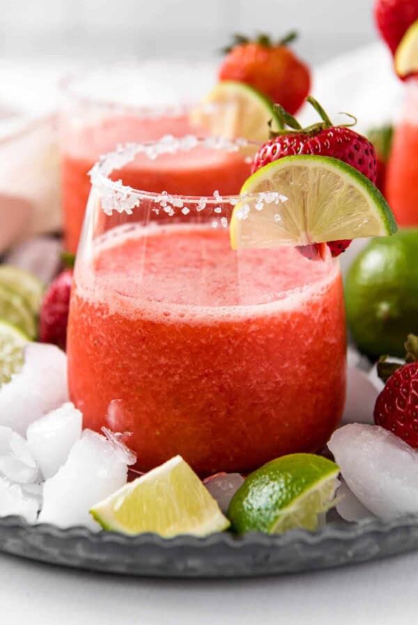 A frozen strawberry margarita in a glass with slice of lime garnish.